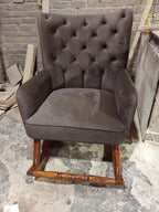 A dark brown tufted velvet armchair with wooden rocking legs, photographed in a workshop.