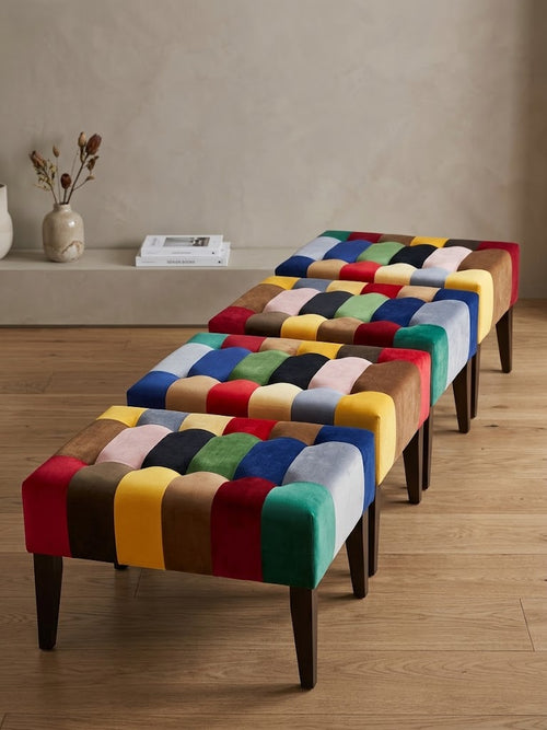 Three matching upholstered bench stools with colorful patchwork cushions and dark wooden legs, arranged on a wood floor in a styled interior room.