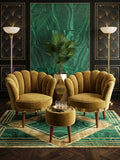 A luxury Art Deco lounge set featuring two scalloped mustard yellow velvet armchairs and a matching round ottoman, arranged on a green and gold patterned rug in front of a green marble wall panel.