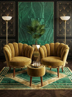 A luxury Art Deco lounge set featuring two scalloped mustard yellow velvet armchairs and a matching round ottoman, arranged on a green and gold patterned rug in front of a green marble wall panel.