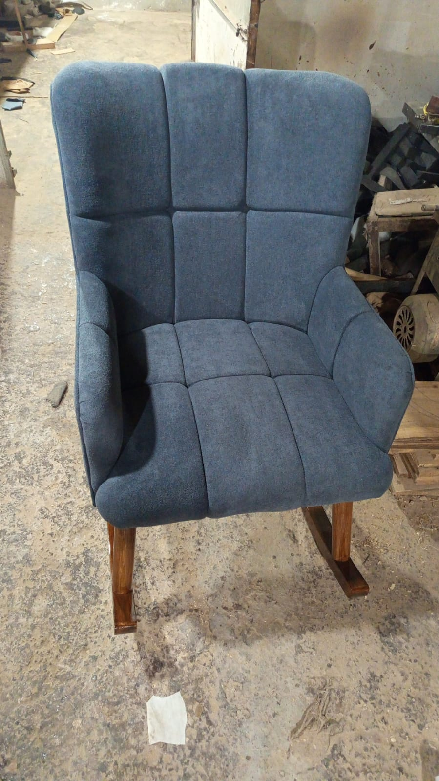 A blue upholstered rocking chair with a high back and wooden rockers, photographed in a workshop.