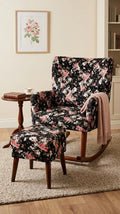 A floral upholstered rocking chair with a matching ottoman in a warm living room setting. The chair and ottoman feature a black background with pink, red, and white floral print, with the chair having dark wood rockers and a light pink throw blanket draped over one arm.