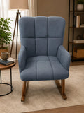 A blue upholstered rocking armchair with a high back, padded channel tufting, and wooden rocking legs, shown in a styled living room setting.