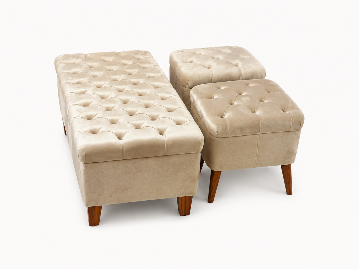 A set of three tufted storage ottomans in a warm beige velvet fabric with dark brown wooden legs, shown on a clean white background.