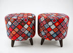 Two round upholstered ottomans with dark wooden legs, featuring a vibrant multicolor patchwork diamond pattern in red, blue, orange, black, and white on a light gray background.