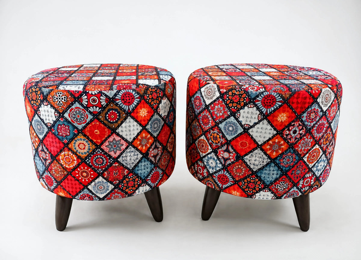 Two round upholstered ottomans with dark wooden legs, featuring a vibrant multicolor patchwork diamond pattern in red, blue, orange, black, and white on a light gray background.