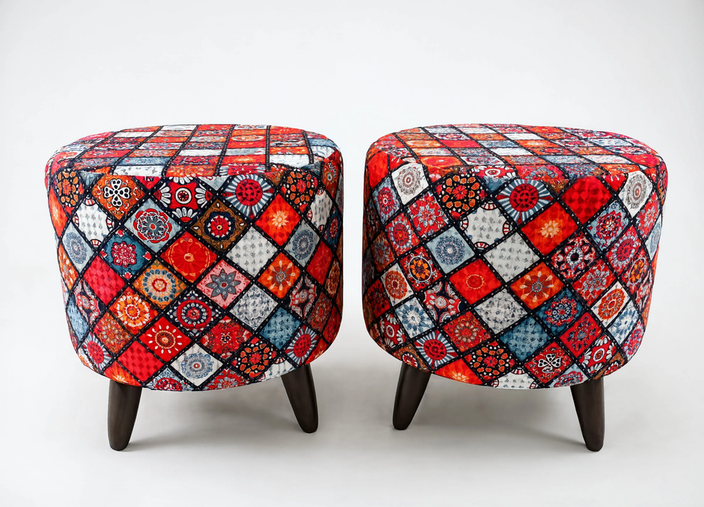 Two round upholstered ottomans with dark wooden legs, featuring a vibrant multicolor patchwork diamond pattern in red, blue, orange, black, and white on a light gray background.