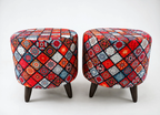 Two round upholstered ottomans with dark wooden legs, featuring a vibrant multicolor patchwork diamond pattern in red, blue, orange, black, and white on a light gray background.