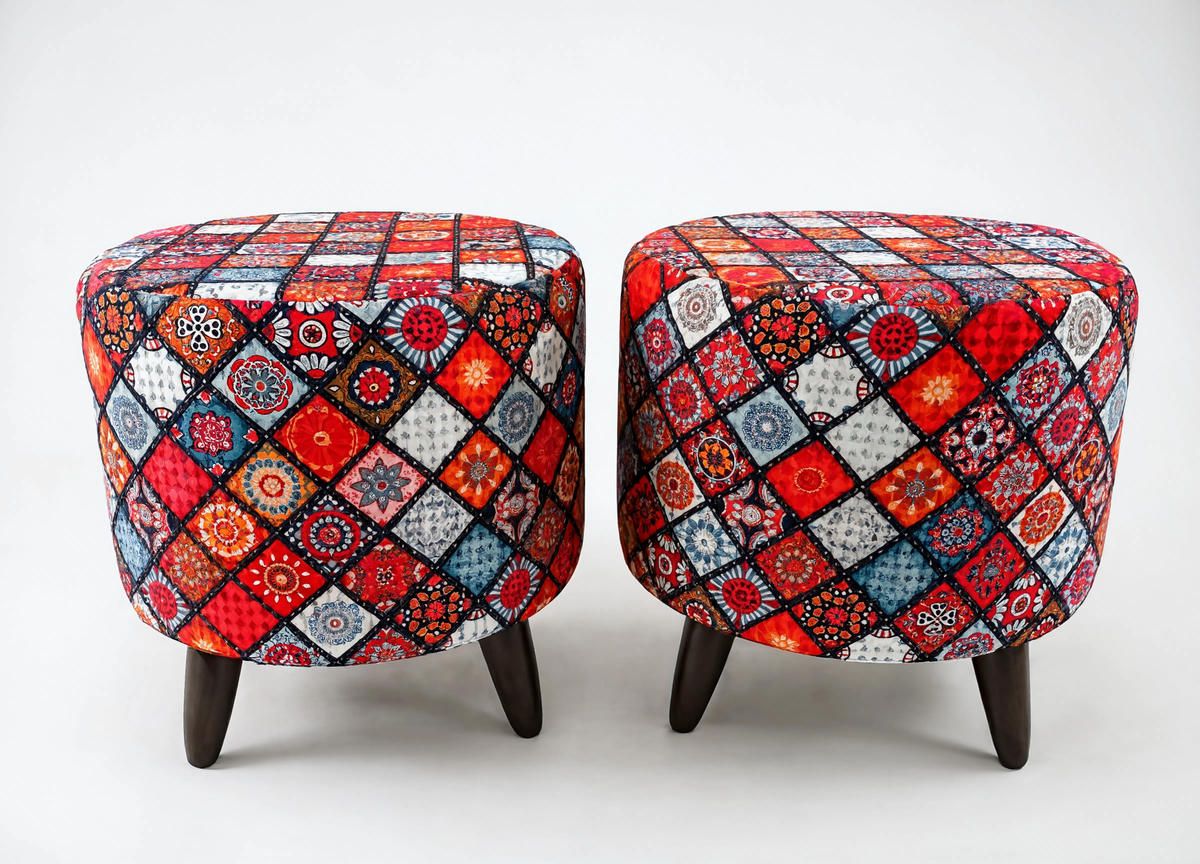 Two round upholstered ottomans with dark wooden legs, featuring a vibrant multicolor patchwork diamond pattern in red, blue, orange, black, and white on a light gray background.
