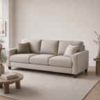 A light beige upholstered three-seat sofa with two matching throw pillows, shown in a minimalist living room setting with a wooden coffee table, a large neutral rug, and soft natural light.