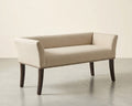An upholstered bench with a light beige textured fabric, dark brown wooden legs, and silver nailhead trim, shown against a neutral studio background.