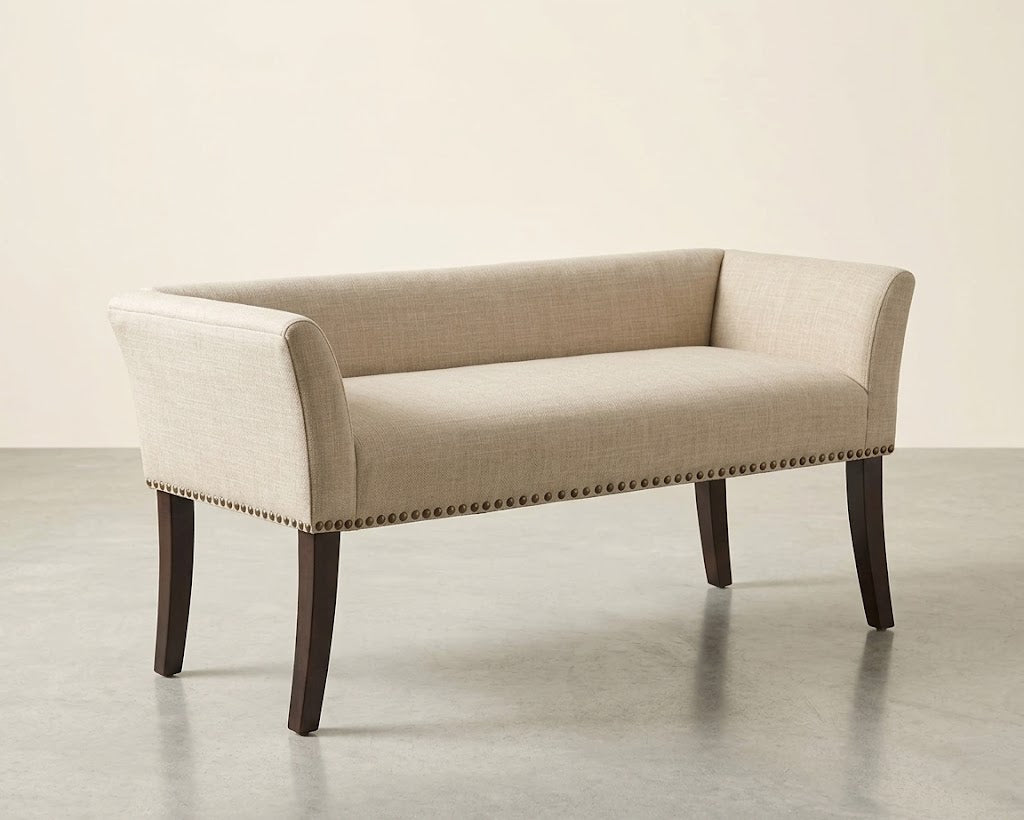 An upholstered bench with a light beige textured fabric, dark brown wooden legs, and silver nailhead trim, shown against a neutral studio background.