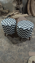 Two round upholstered stools with black and white chevron-patterned fabric and dark wooden legs, photographed in a workshop or furniture shop with wood scraps and machinery in the background.