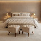 A staged bedroom scene with a bed dressed in cream bedding, two matching upholstered ottomans at the foot of the bed, side tables with lit lamps, and a warm beige wall and carpet.